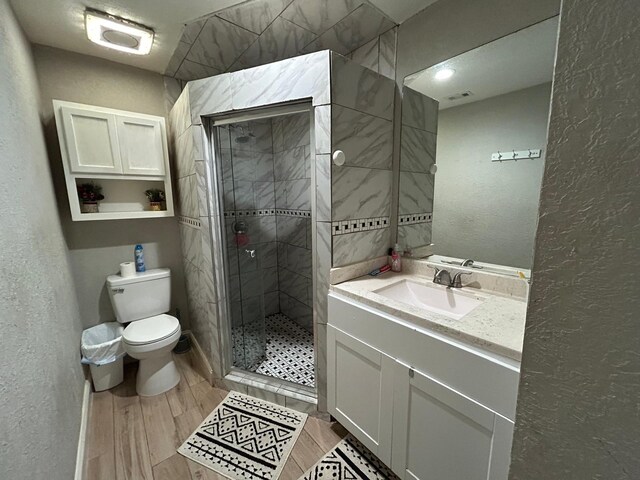 bathroom with a stall shower, wood finished floors, vanity, toilet, and a textured wall