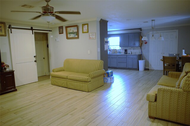 living area featuring a ceiling fan, visible vents, a barn door, ornamental molding, and light wood-style flooring
