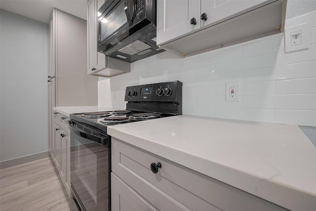kitchen featuring light wood-style floors, backsplash, black appliances, and light stone countertops