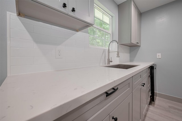 kitchen featuring baseboards, tasteful backsplash, light stone counters, a sink, and light wood-style flooring