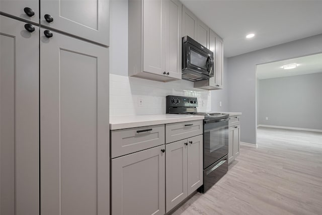 kitchen featuring tasteful backsplash, light wood-type flooring, light countertops, baseboards, and black appliances