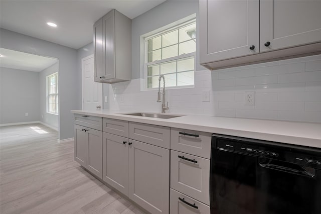 kitchen with a sink, light wood finished floors, dishwasher, baseboards, and tasteful backsplash