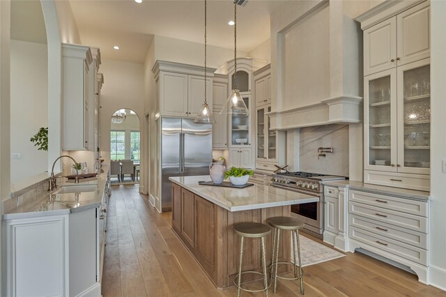 kitchen with a center island, wall chimney exhaust hood, a sink, light wood finished floors, and premium appliances
