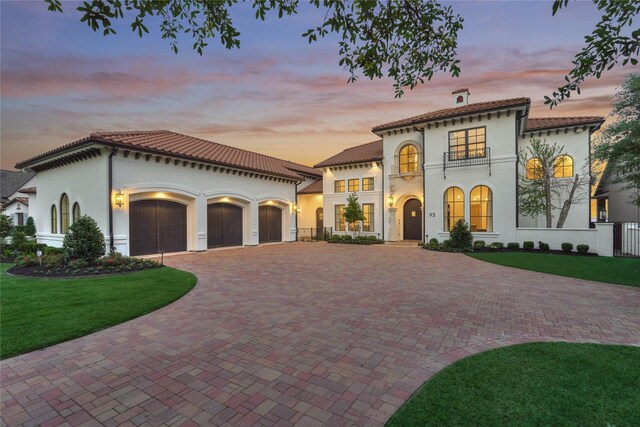 mediterranean / spanish home with a garage, decorative driveway, a balcony, a yard, and stucco siding