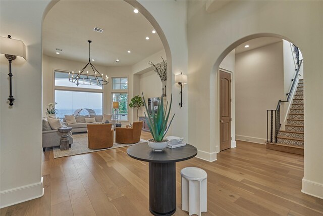 entrance foyer with arched walkways, visible vents, light wood-style flooring, and an inviting chandelier