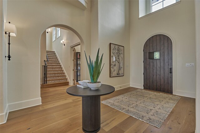 entryway featuring baseboards, arched walkways, a towering ceiling, and wood finished floors