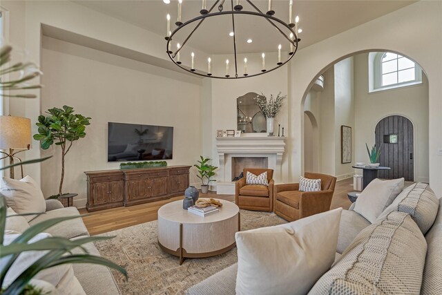 living room featuring a towering ceiling, wood finished floors, a fireplace with raised hearth, arched walkways, and a notable chandelier