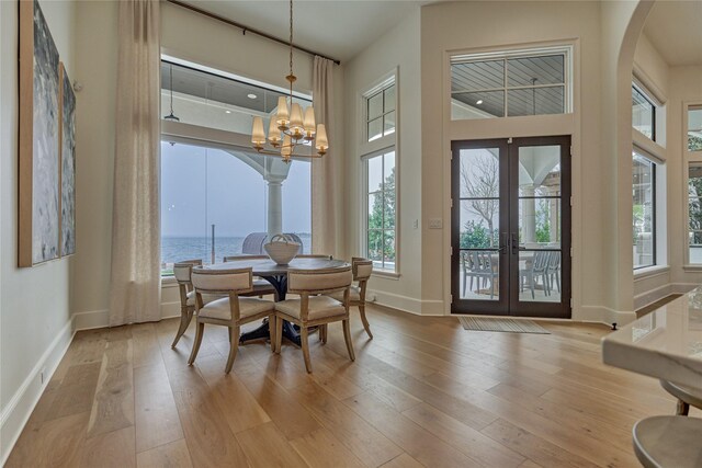 dining space featuring arched walkways, a chandelier, french doors, light wood-style flooring, and baseboards