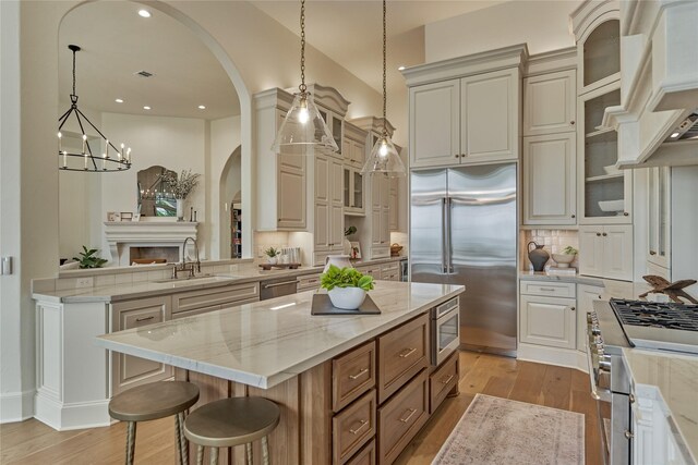 kitchen featuring a kitchen island, arched walkways, a sink, built in appliances, and light wood-style flooring