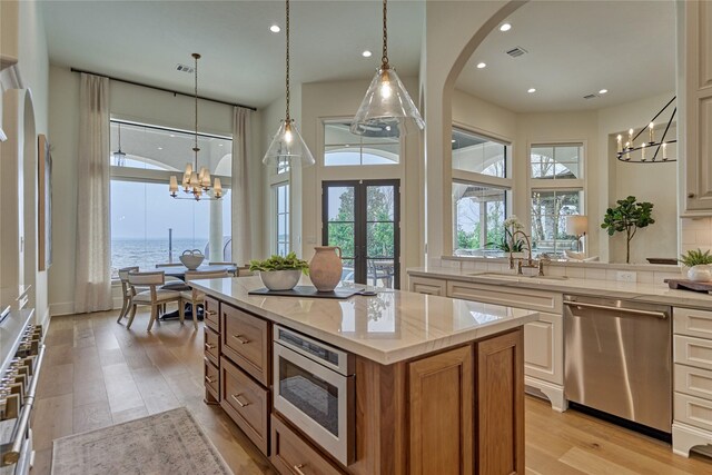 kitchen featuring appliances with stainless steel finishes, arched walkways, a sink, a notable chandelier, and light wood-style floors