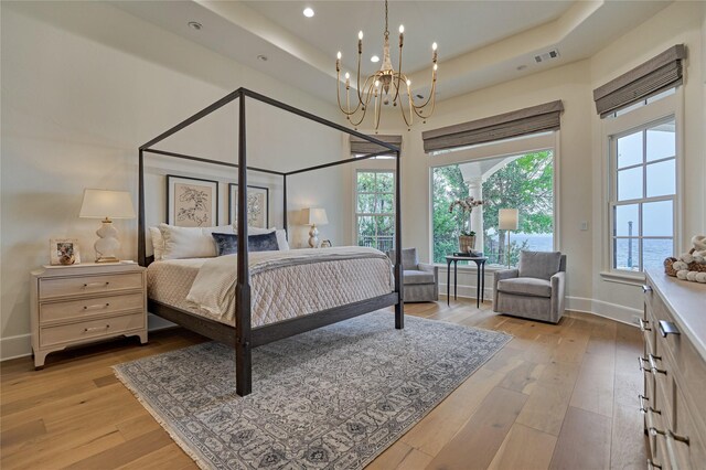bedroom featuring baseboards, light wood-style flooring, a chandelier, and a tray ceiling