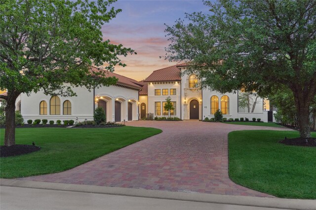 mediterranean / spanish home featuring an attached garage, decorative driveway, stucco siding, and a yard