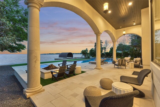 patio terrace at dusk featuring a water view, an outdoor fire pit, and an outdoor pool