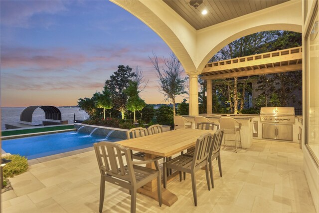 pool at dusk with an outdoor kitchen, outdoor dining area, a patio area, and area for grilling