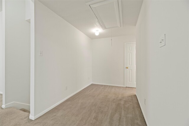 empty room featuring baseboards, light colored carpet, and attic access