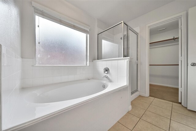 full bath with a walk in closet, a shower stall, tile patterned floors, and a garden tub