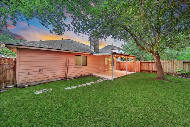 back of property at dusk featuring a yard, a patio, a chimney, and a fenced backyard