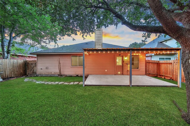 back of house at dusk featuring a patio, a fenced backyard, a lawn, and a chimney