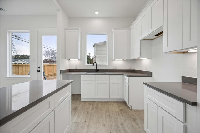 kitchen with dark countertops, recessed lighting, white cabinets, a sink, and light wood finished floors