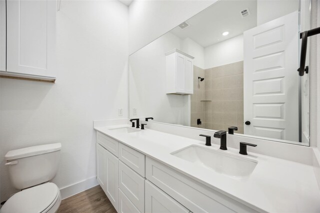 full bath with toilet, a tile shower, a sink, and wood finished floors