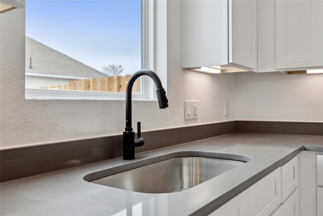 room details featuring a sink, a textured wall, white cabinets, and dark countertops