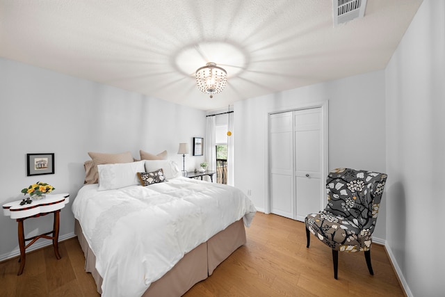 bedroom with a notable chandelier, light wood-style flooring, visible vents, and a closet