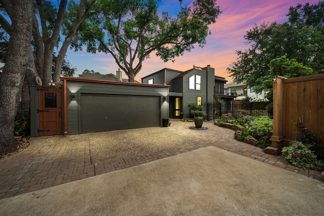 view of front of house featuring decorative driveway, an attached garage, fence, and a chimney