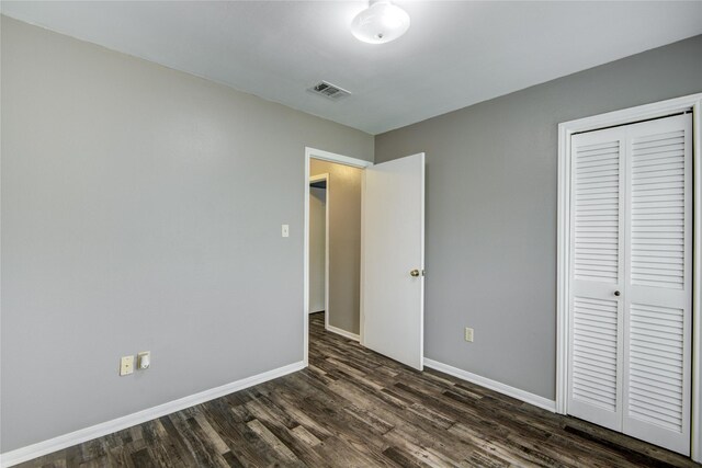 unfurnished bedroom featuring baseboards, a closet, dark wood-style flooring, and visible vents