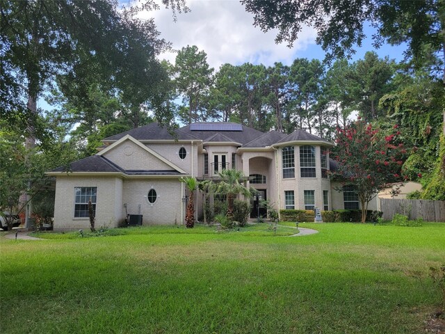 back of property featuring cooling unit, fence, a yard, and solar panels