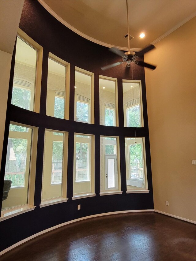 spare room with crown molding, wood finished floors, baseboards, a high ceiling, and recessed lighting