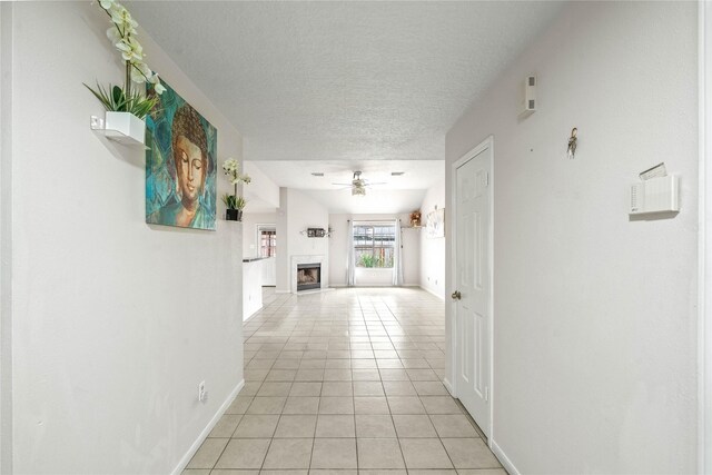 hallway with a textured ceiling, baseboards, and light tile patterned flooring