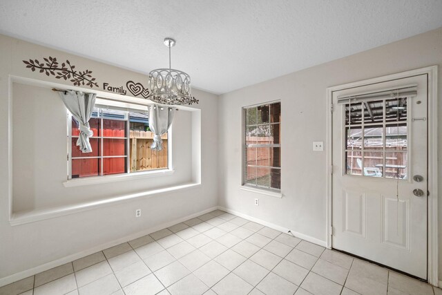 unfurnished dining area with a textured ceiling, a notable chandelier, baseboards, and tile patterned floors