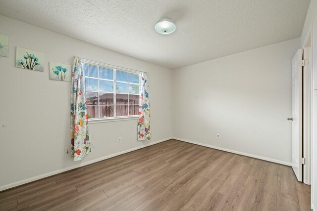 spare room with a textured ceiling, baseboards, and wood finished floors