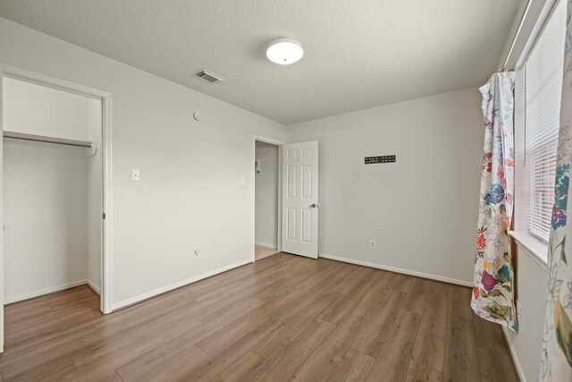 unfurnished bedroom featuring visible vents, baseboards, wood finished floors, and a closet