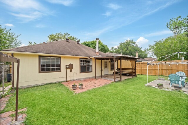 rear view of property with central AC unit, a fenced backyard, a yard, a patio, and a shingled roof
