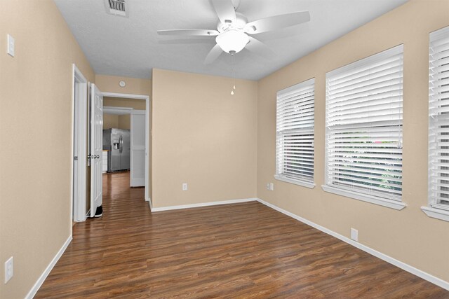 spare room with dark wood-style flooring, ceiling fan, visible vents, and baseboards