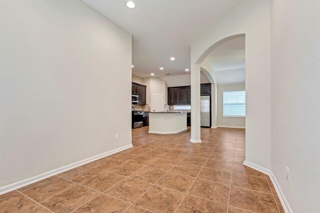 unfurnished living room featuring light tile patterned floors, arched walkways, baseboards, and recessed lighting
