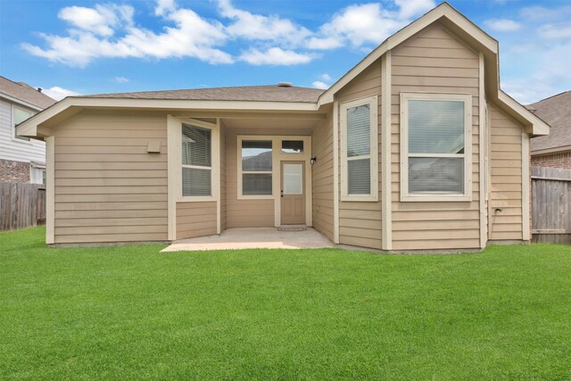 back of house with a lawn, a shingled roof, and fence