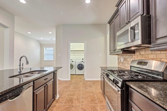 kitchen with independent washer and dryer, a sink, dark stone counters, stainless steel appliances, and tasteful backsplash