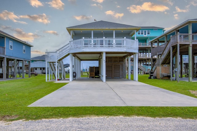 back of house at dusk featuring a lawn, driveway, stairway, and a carport