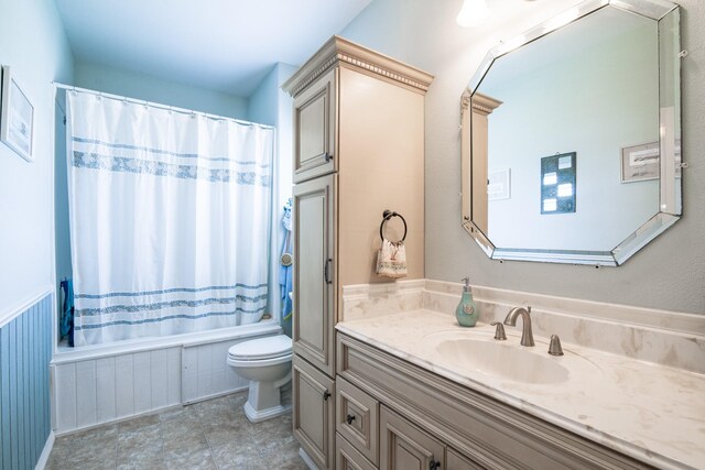full bath featuring toilet, shower / bathtub combination with curtain, a wainscoted wall, and vanity
