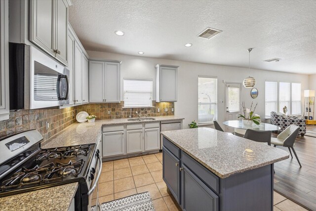 kitchen with a textured ceiling, gray cabinets, tasteful backsplash, a sink, and stainless steel appliances