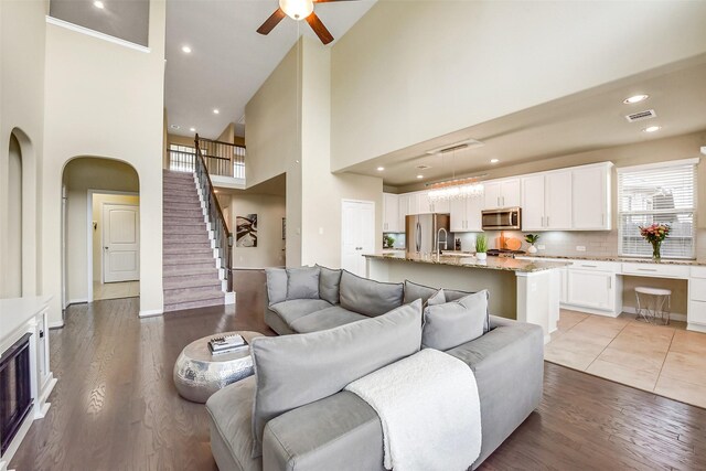 living room featuring visible vents, light wood-style floors, ceiling fan, and a high ceiling