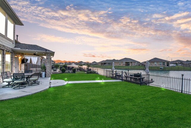 yard at dusk with a patio, a water view, fence, and a residential view