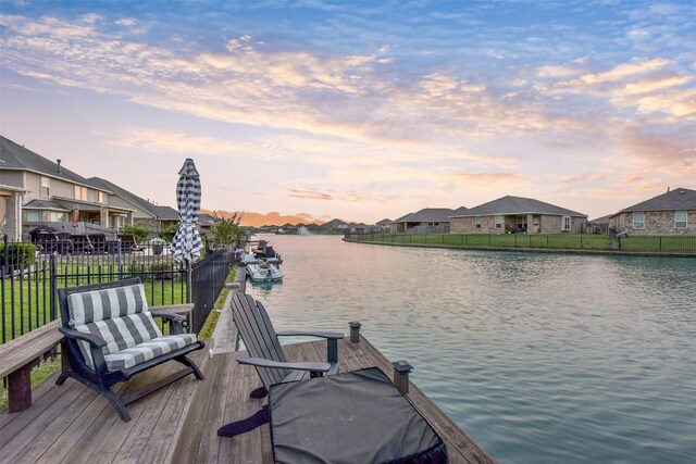 view of dock featuring a water view, fence, and a residential view