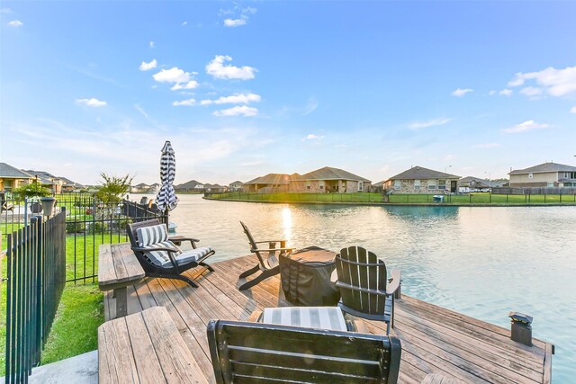 view of dock featuring a water view, fence, and a residential view