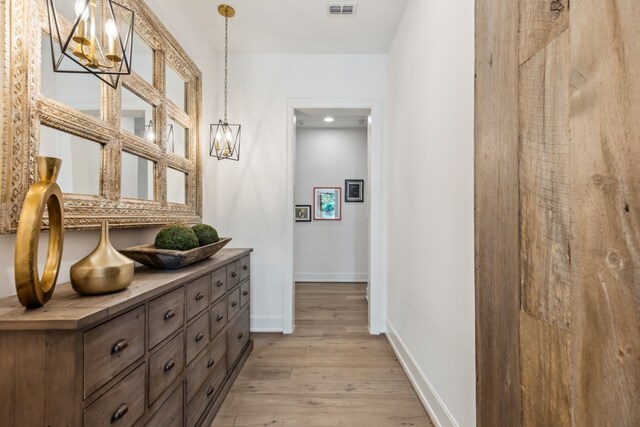hall featuring light wood-type flooring, baseboards, visible vents, and an inviting chandelier