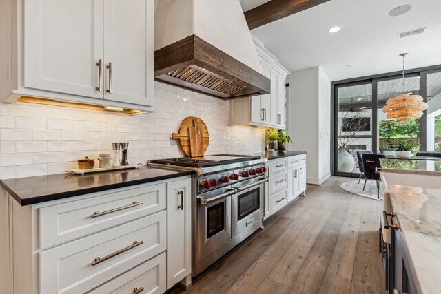 kitchen featuring backsplash, double oven range, visible vents, wood finished floors, and premium range hood