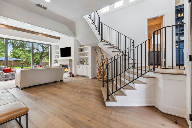 stairs with visible vents, built in shelves, baseboards, a warm lit fireplace, and hardwood / wood-style floors