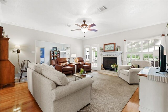 living room featuring ceiling fan, ornamental molding, light wood finished floors, and visible vents
